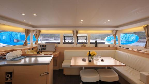 The bright and modern salon of a Lagoon 560 catamaran features a cozy seating area with a dining table, surrounded by la